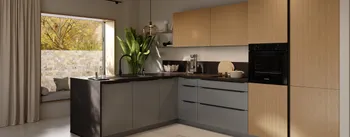 Moderne L‑Küche mit matten grauen Unterschränken, hellen Holzfronten und schwarzer Arbeitsplatte; Insel mit Spülbecken und schwarzem Wasserhahn, integrierter Bosch‑Backofen, Pendelleuchte, große Fensterbank mit Kissen, grüne Zimmerpflanze.